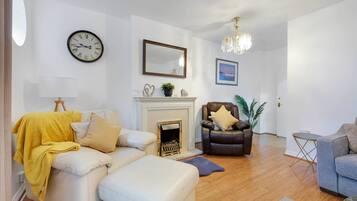 A living room with a sofa, armchair, fireplace, and a clock on the wall.