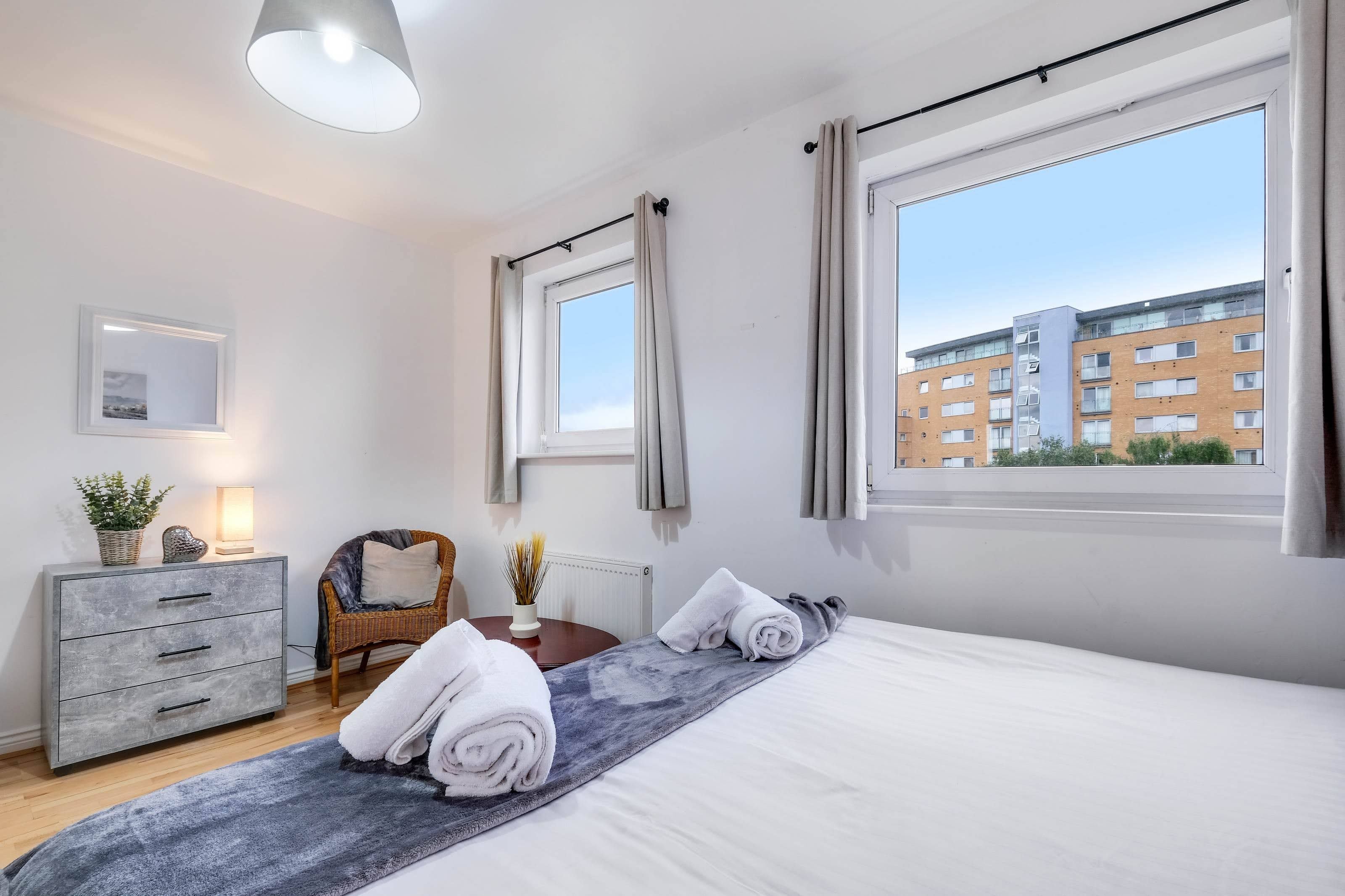 Een moderne slaapkamer met een groot bed, een dressoir, een stoel en een raam met uitzicht op een gebouw.