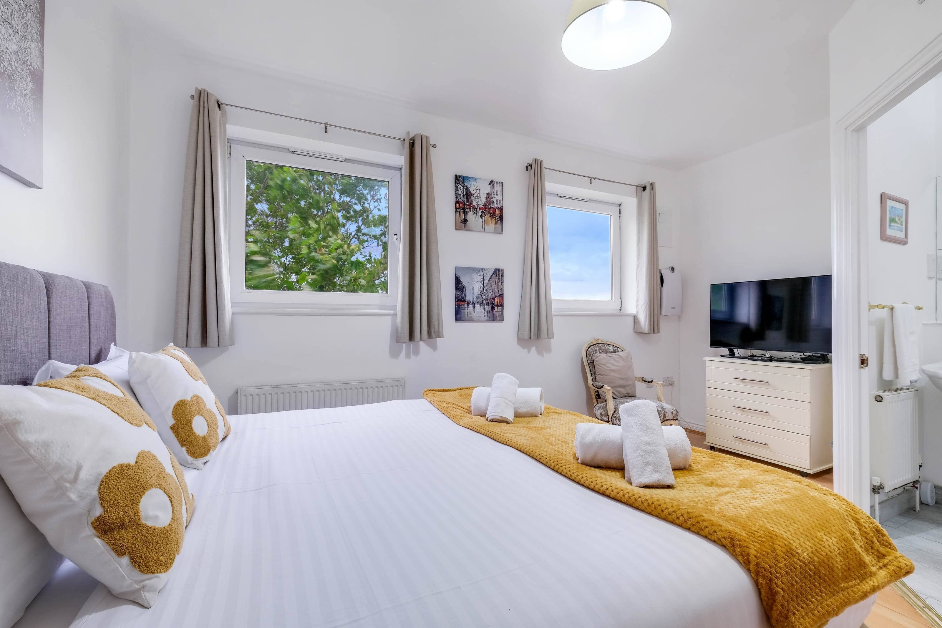 Een hotelkamer met een groot bed, twee ramen met gordijnen, een televisie, een kast en een radiator.