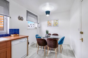 Una cocina compacta con encimera de madera, lavavajillas y un comedor con mesa de vidrio y sillas acolchadas.