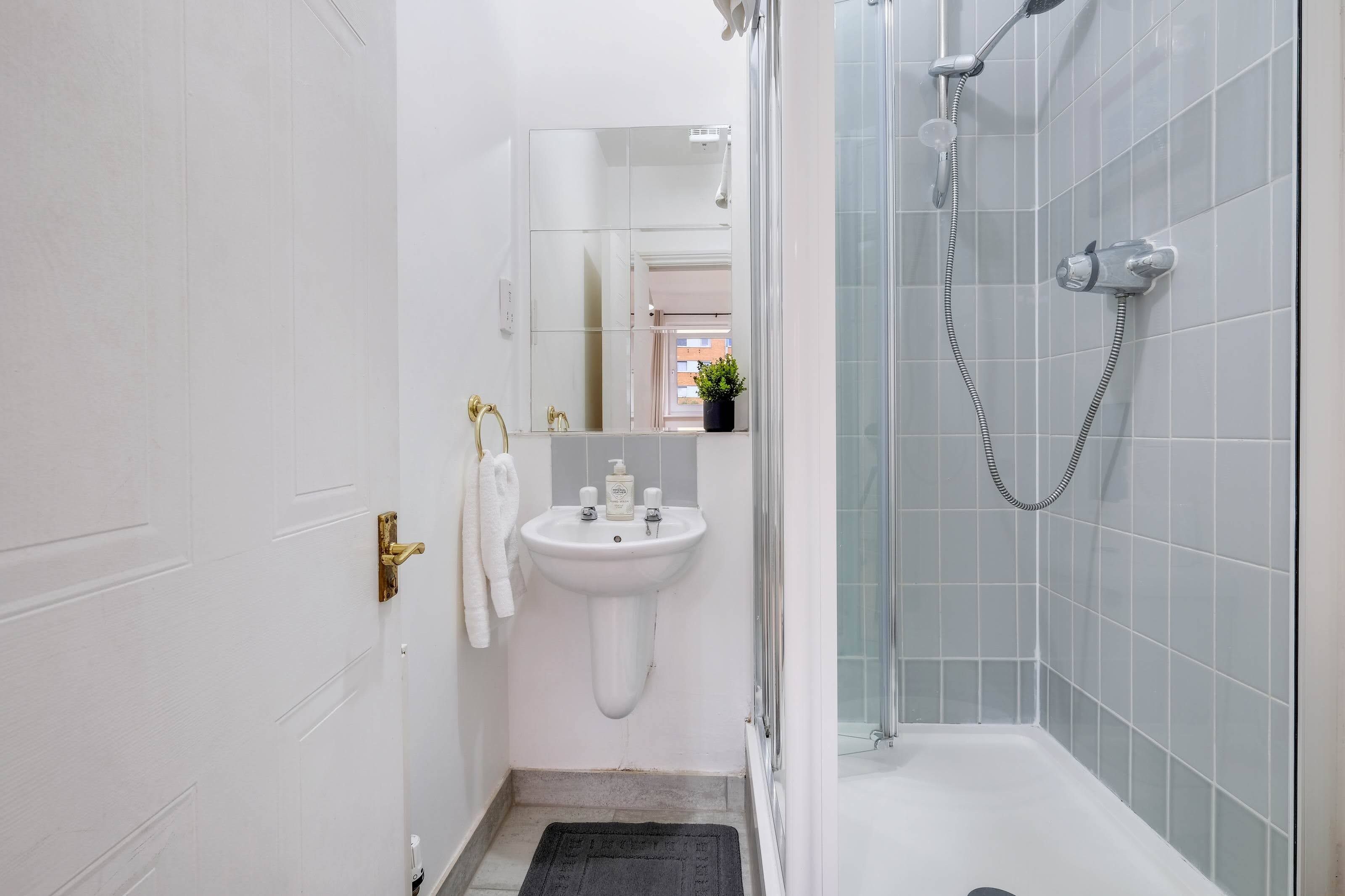 Une salle de bain moderne avec un lavabo blanc, une douche en verre et une petite plante en pot posée sur le rebord de la fenêtre.