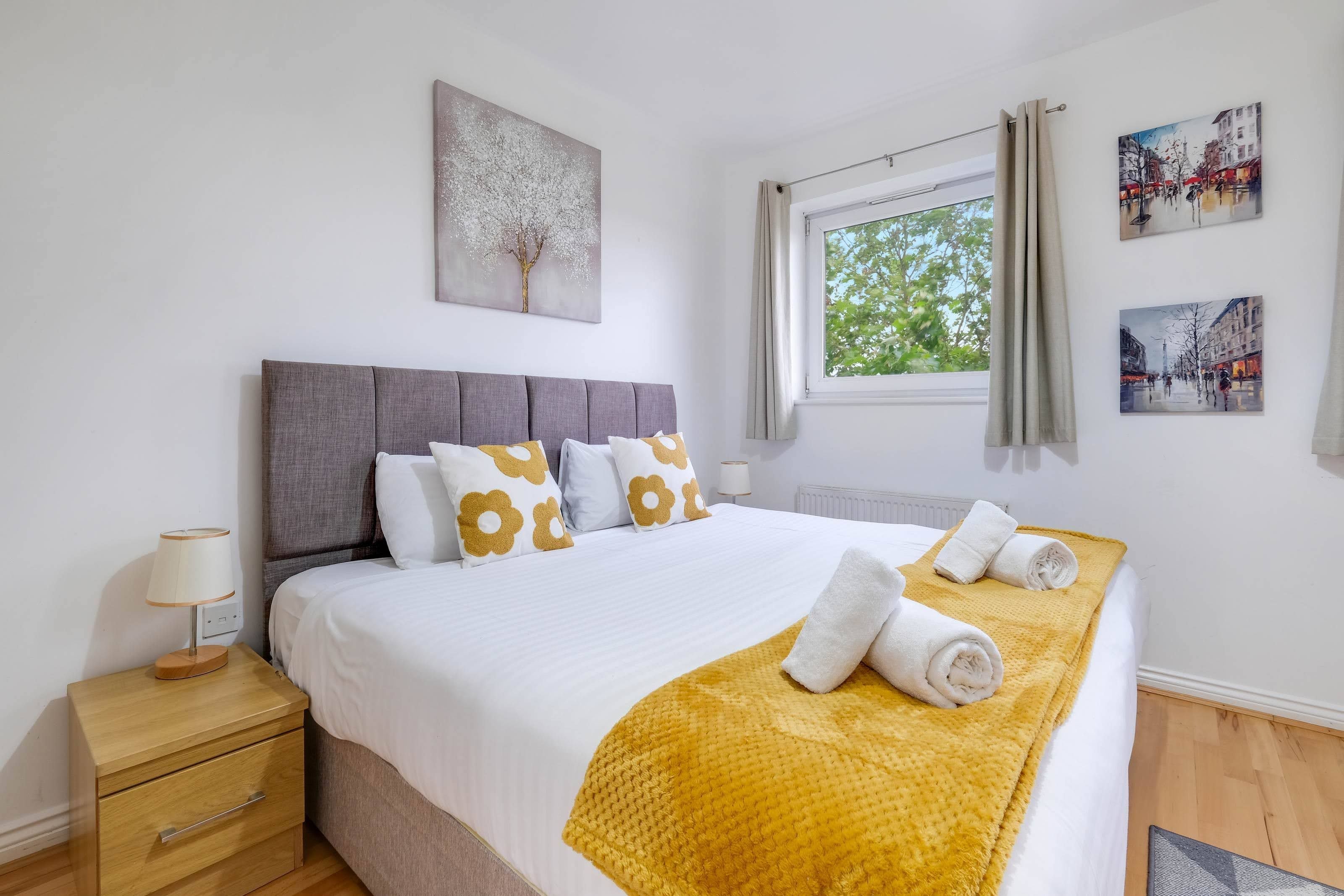 Une chambre d’hôtel moderne avec un grand lit, une table de chevet, une lampe et des œuvres d’art accrochées aux murs.