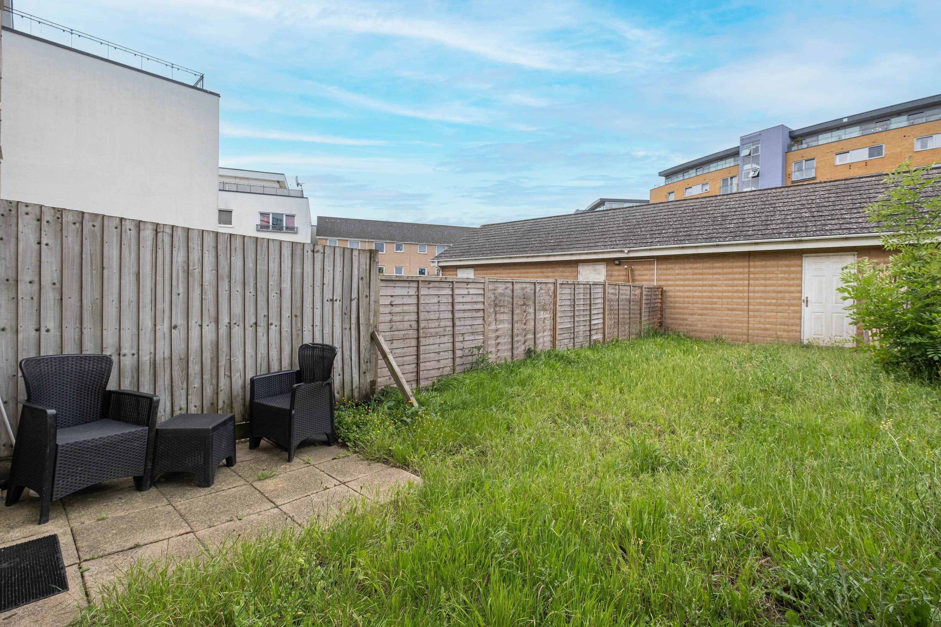 A backyard with a wooden fence, two wicker chairs, and a grassy area.