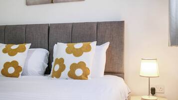 A neatly made bed with a grey upholstered headboard, white bedding, and decorative pillows with a gold pattern.
