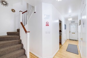 Una escalera con barandillas de madera y peldaños alfombrados que conduce a una habitación con paredes blancas, una puerta y una lámpara.
