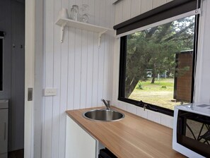 Cozinha com pia de aço inoxidável, bancada de madeira e janela com vista para árvores.