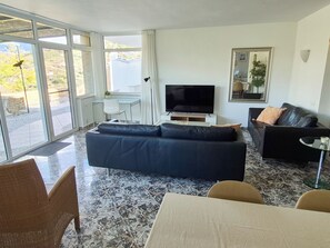 Ein Wohnzimmer mit einer Couch, einem Fernseher, einem Esstisch und einem Sessel.