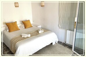 Habitación de hotel con una cama grande, dos almohadas, una toalla enrollada y una puerta de ducha de vidrio.
