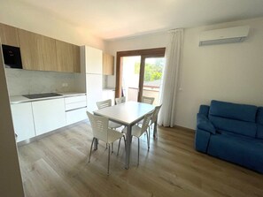 A modern kitchen with a dining area, a blue sofa, and a sliding glass door to the outdoors. - Serenity accommodation by the sea (Bibione)