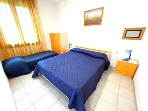 Ein Hotelzimmer mit zwei Betten, einem Schreibtisch, einem Stuhl, einem Kleiderschrank und einem Bild an der Wand.