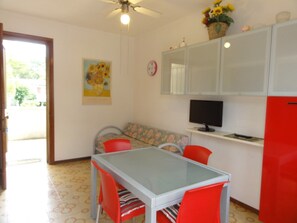 Uma cozinha compacta com mesa, cadeiras, geladeira e televisão.
