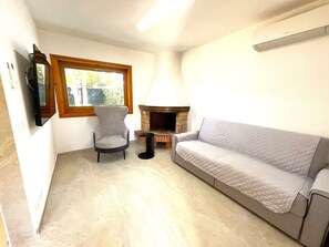 A living room with a stone fireplace, a grey armchair, and a grey sofa. - Holiday home with garden in Bibione Pineda (Bibione Pineda)