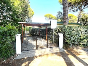 Uma entrada com portão e galeria coberta, cercada por vegetação e árvores.