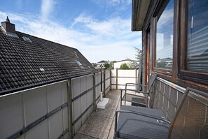En balkong med en metallstol, ett litet bord och utsikt över de omkringliggande husen.