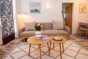 A cozy living room with a sofa, two side tables, a vase with flowers, and a painting on the wall. - Cozy Vacation Rental 1 at Haus Kuhlmann (Büsum)