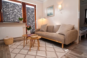 A cozy living room with a sofa, a small table, a lamp, a radiator, and a window with a view. - Cozy Vacation Rental 1 at Haus Kuhlmann (Büsum)