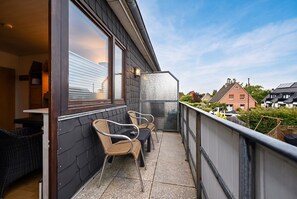 Ein Balkon mit Korbstühlen, einem Tisch und Blick auf Häuser.