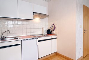 Kompakti keittiö, jossa on valkoiset kaapit, ruostumattomasta teräksestä valmistettu pesuallas ja kahvinkeitin työtasolla.