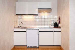 Eine kleine Küche mit weißen Schränken, einer Edelstahl-Spüle, einer Kaffeemaschine und einem Geschirrspüler.