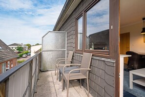 Een balkon met rieten stoelen en een tafel, uitkijkend op een woonstraat.