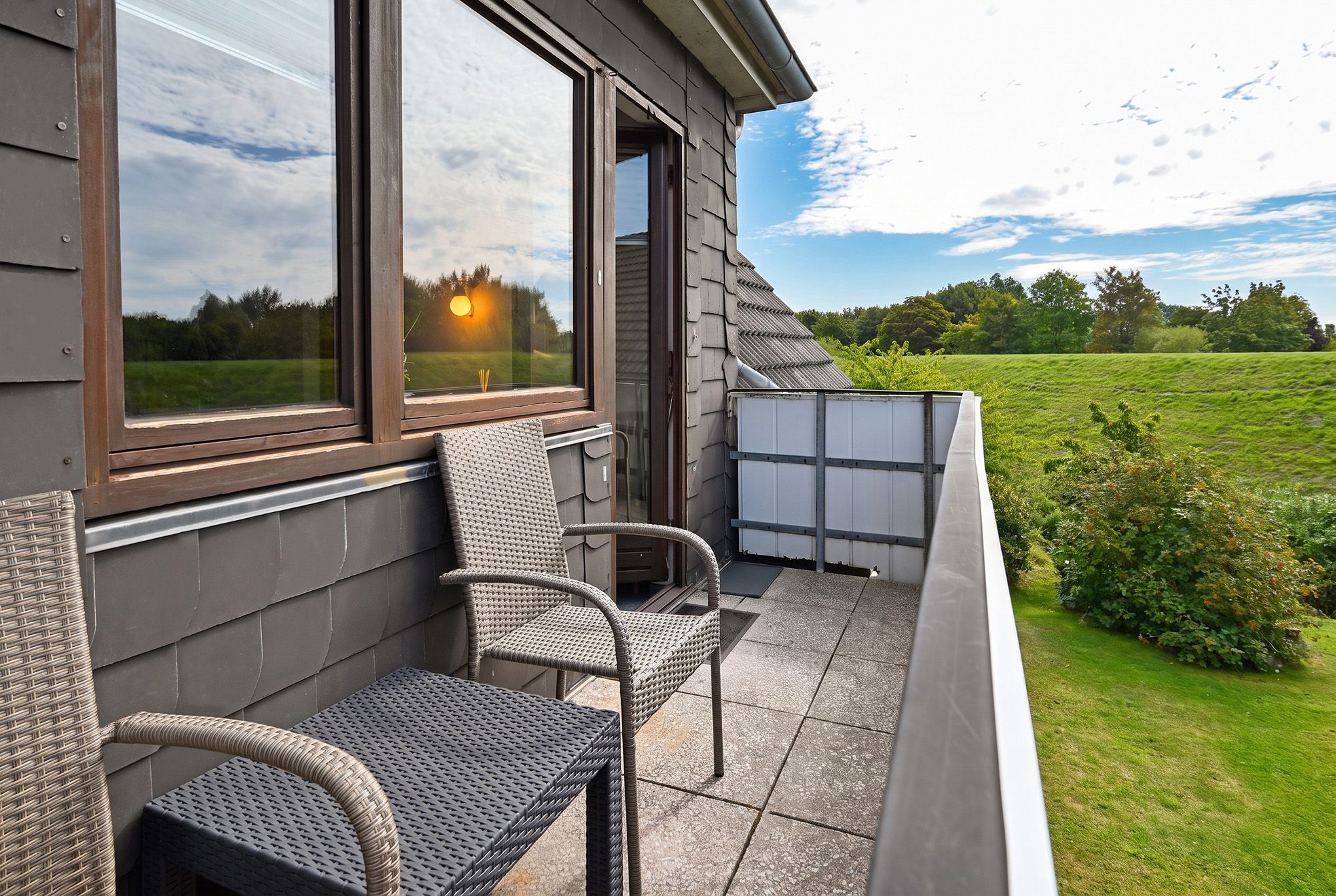 En balkon med fletmøbler og udsigt over et grønt græsareal.