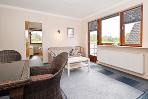 Ein Zimmer mit Esstisch, Korbstühlen, einer Couch, einem Fenster mit Aussicht und einer Heizung.