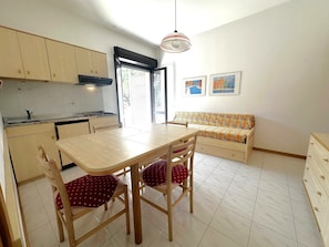 A compact kitchen with a dining area, a sofa, and a view of the outside. - Central flat 250m from beach (Bibione)