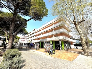A multi-story building with a ground-level entrance, a covered outdoor seating area, and a bicycle parking area. - Central flat 250m from beach (Bibione)