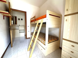 Ein Stockbett mit einer Leiter, einem Schreibtisch und einem Kleiderschrank in einem Raum mit Fliesenboden.