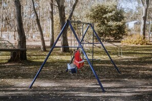 Eine Schaukel mit Metallgestell und roter Sitzfläche in einem Park.