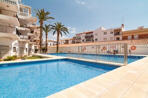 A swimming pool with a tiled deck, surrounded by buildings and palm trees. - Comfortable Apartment in Nerja (Nerja)