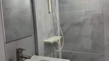 Un baño con un lavamanos blanco, un espejo y una cabina de ducha.
