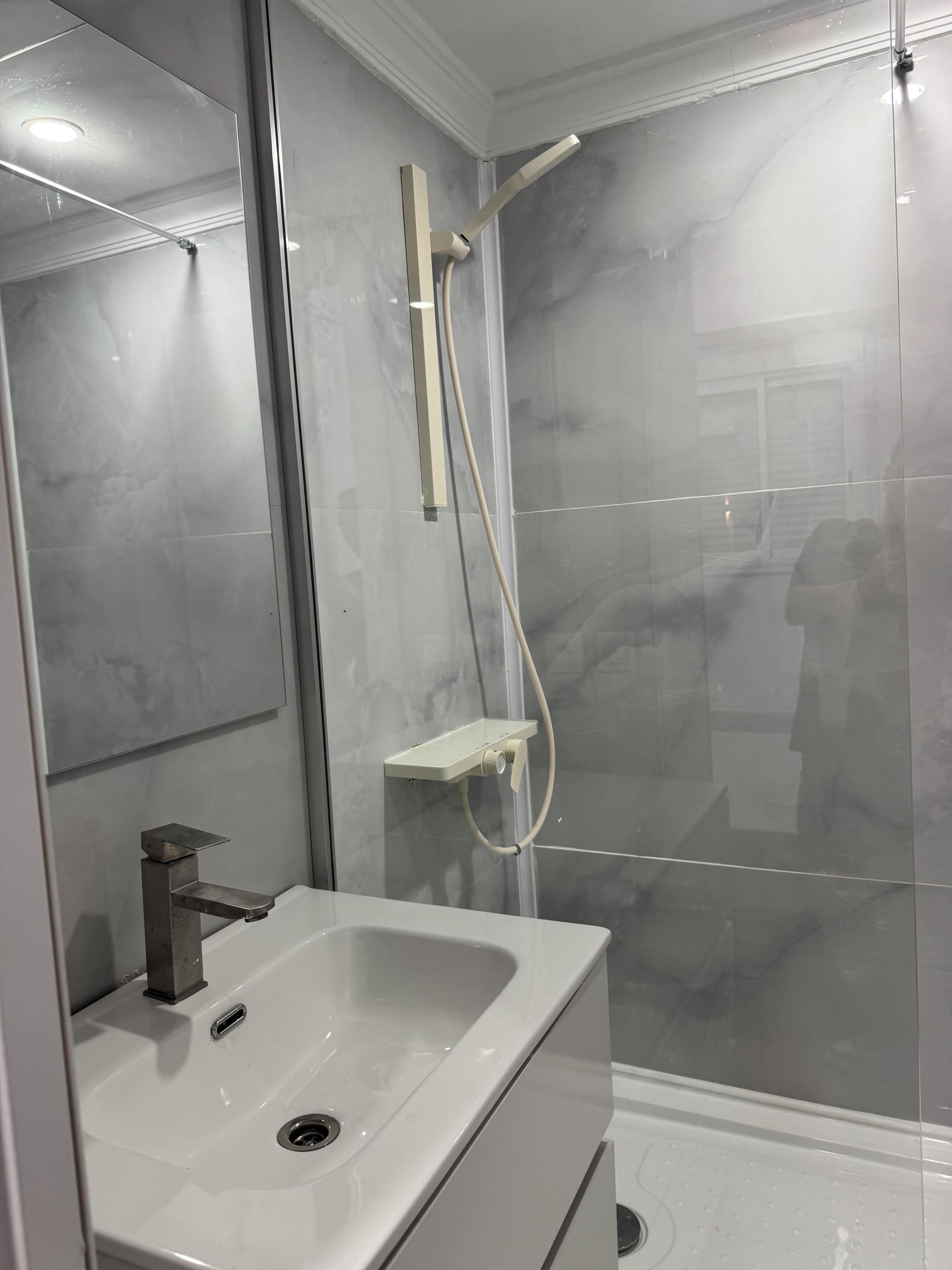 A bathroom with a white sink, a mirror, and a shower enclosure.