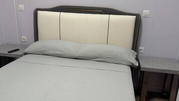 Een bed met hoofdeinde, twee nachtkastjes en een lichtschakelaar aan de muur.