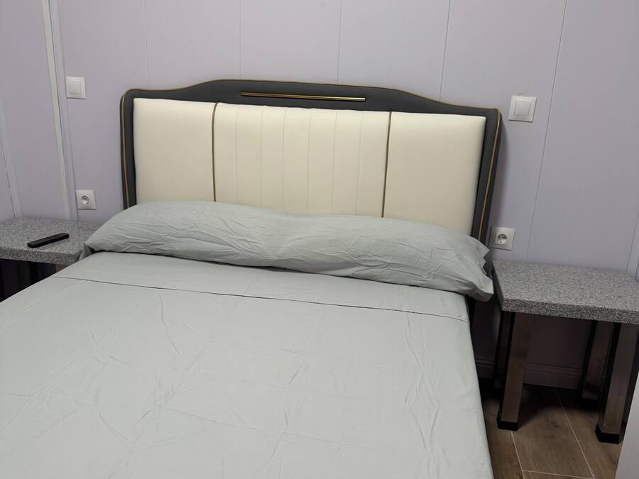 Una cama con cabecera, dos mesitas de noche y un interruptor de luz en la pared.