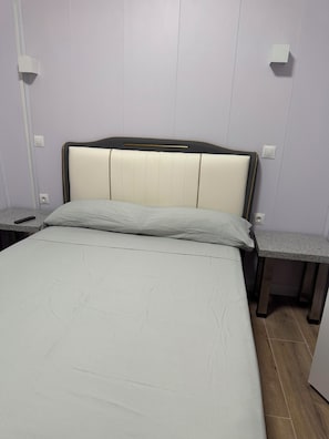 A bed with a headboard, two bedside tables, and a light switch on the wall.
