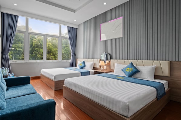Habitación de hotel con dos camas, un sofá, una mesita de noche y un amplio ventanal con cortinas.