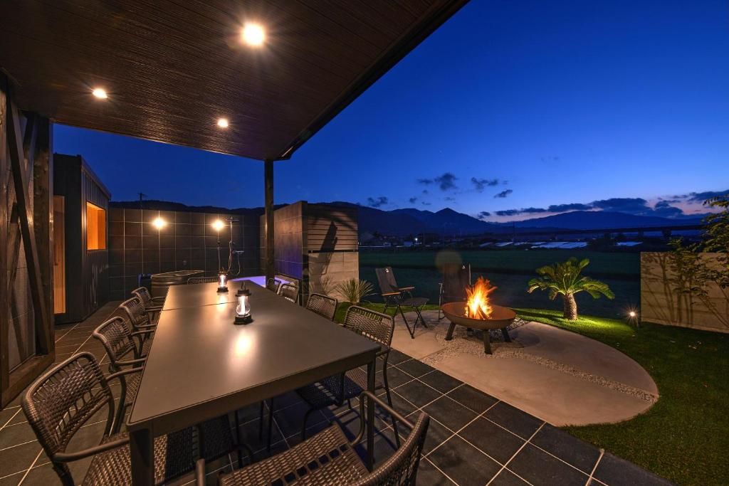 An outdoor dining area with a table and chairs, a fire pit, and a view of mountains at dusk.