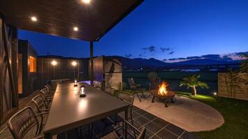 An outdoor dining area with a table and chairs, a fire pit, and a view of mountains at dusk.