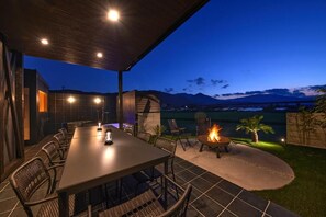 An outdoor dining area with a table and chairs, a fire pit, and a view of mountains at dusk. - SUITE VILLA -AOI- (Takashima-shi)