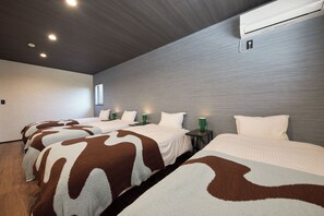 A hotel room with four beds, each with a unique patterned bedspread, a modern air conditioning unit, and a small table with a green lamp. - SUITE VILLA -AOI- (Takashima-shi)
