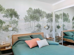 Ein Schlafzimmer mit einem Bett, Kissen, einem Nachttisch, einem Spiegel und einem Wandbild.
