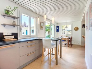 Eine moderne Küche mit einer zentralen Kochinsel, Holzkästen und einem Esstisch für vier Personen.