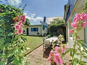 A patio with a table and chairs, a grassy lawn, and a building with a satellite dish. - Cozy, Renovated Seaside Home by Groom* (Ploemeur)