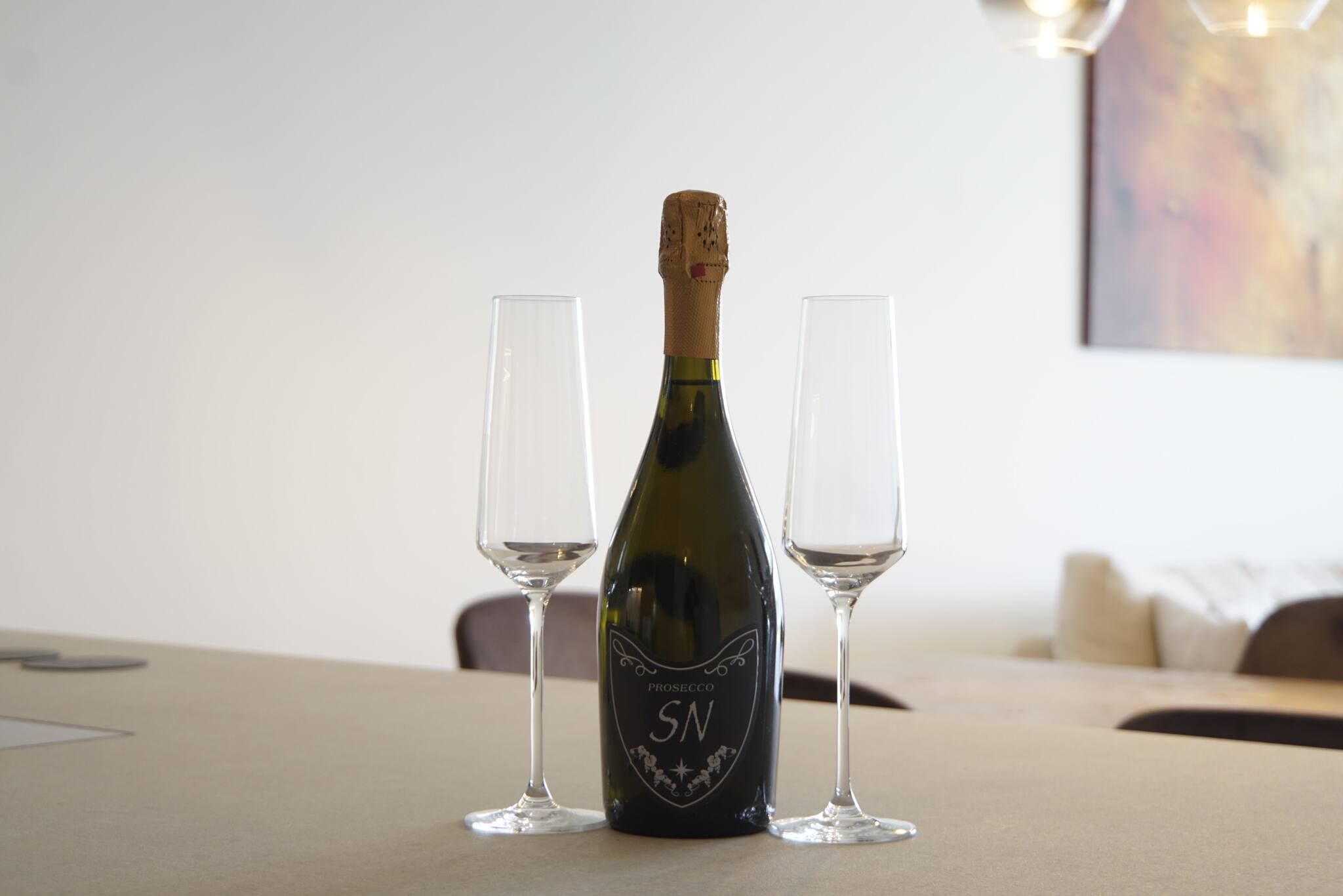 A bottle of Prosecco SN wine with two empty glasses on a table.