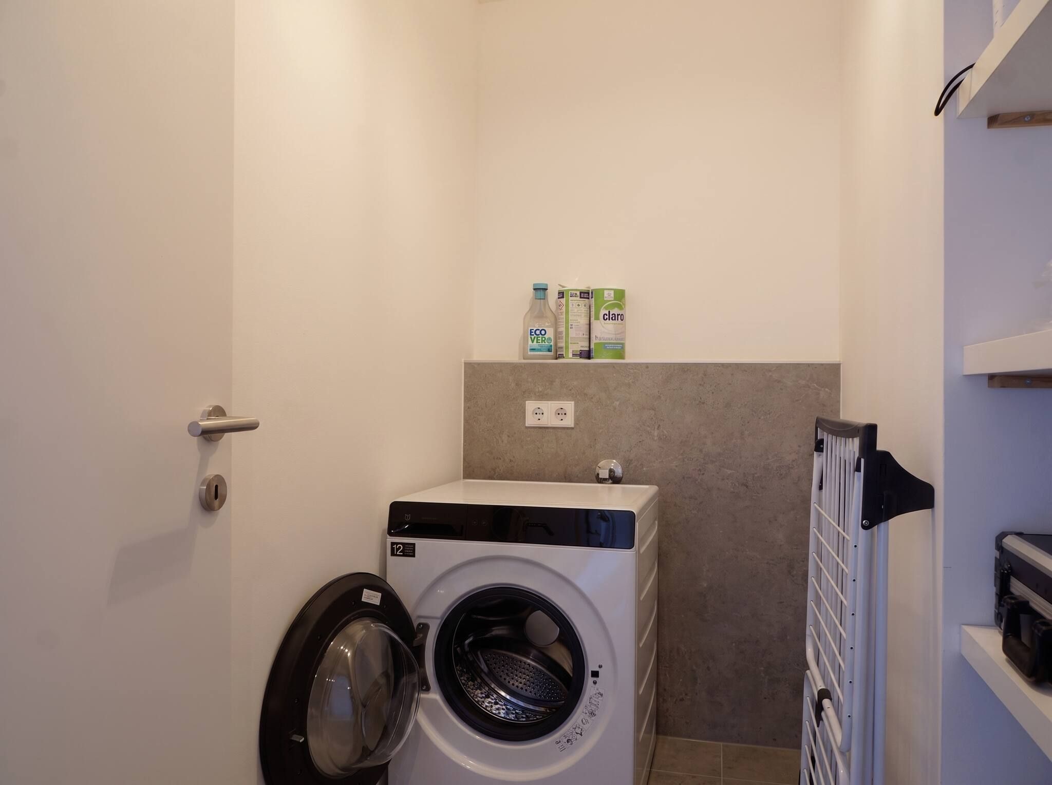 A compact laundry room with a front-loading washing machine, a dryer, and a shelf with cleaning products.