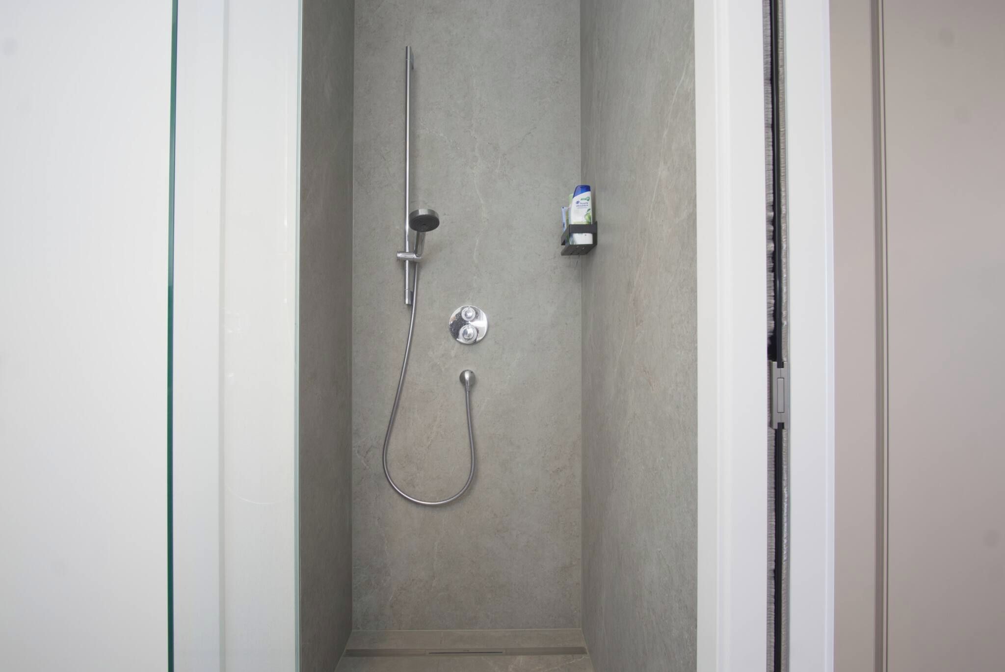 Eine Dusche mit Duschbrause, Wandarmatur und Seifenspender.