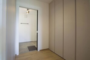 A hallway with a door leading to a room, a light fixture above the door, and a small rug on the floor.