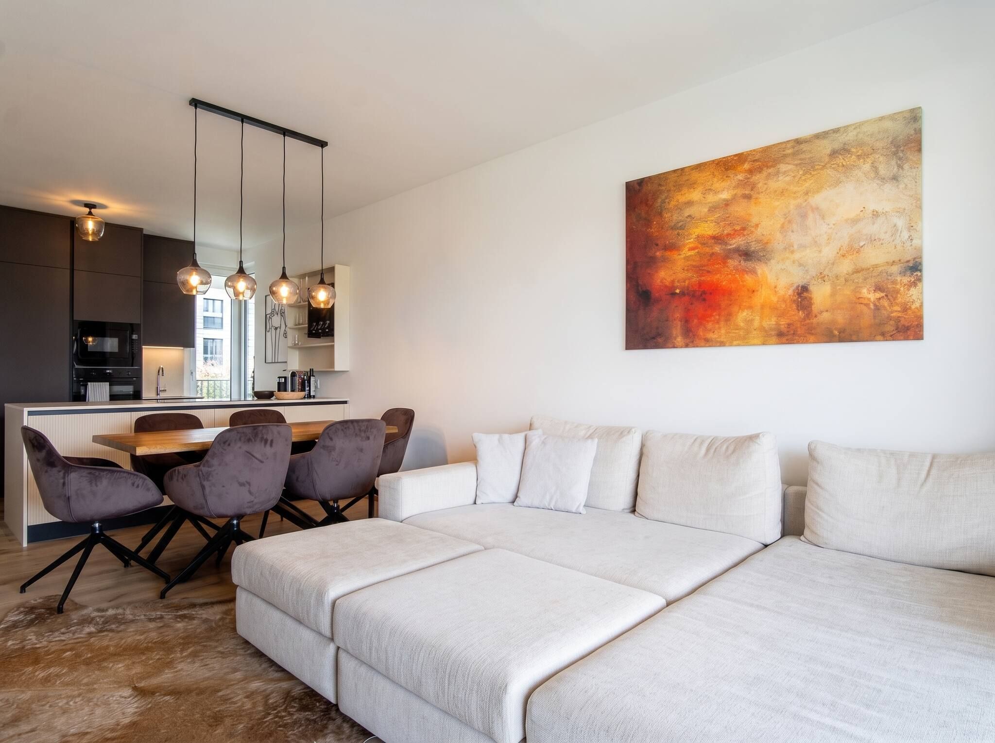 Ein modernes Wohnzimmer mit einer großen Couch, einem Essbereich mit Stühlen und einer Küche im Hintergrund.