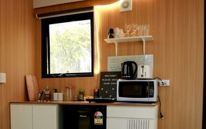A compact kitchenette with a microwave, a coffee maker, and a shelf with glasses and cups.